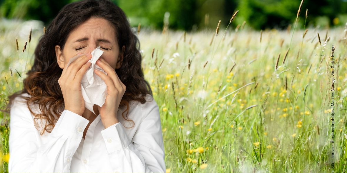 Niesende Frau mit Taschentuch. Wiese mit blühenden Gräsern und Wildblumen im Hintergrund zum Thema Heuschnupfen und Pollenallergie - 10 Tipps, die wirklich helfen.